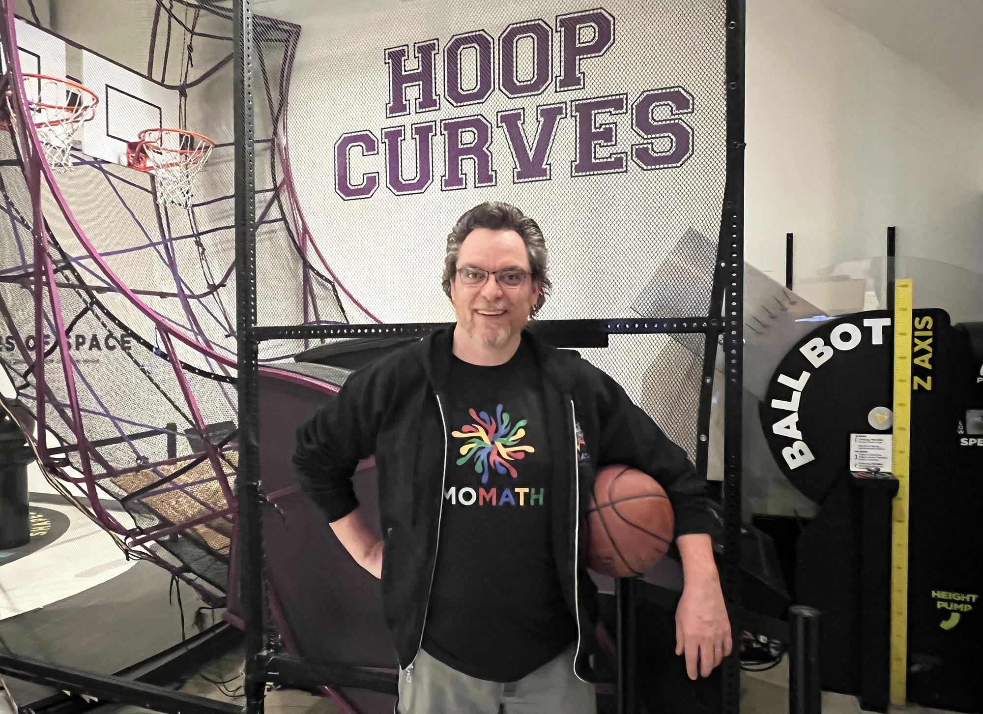 Tim Chartier is the 2022-23 Distinguished Visiting Professor at the National Museum of Mathematics (MoMath) in New York City. Visitors to the museum can smoothly ride a square-wheeled tricycle; extend their arms and become fractal trees; and track data while shooting a basketball at the Hoop Curves exhibit, which is pictured here. Photo courtesy of MoMath.